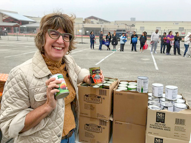 Chief Sustainability Officer Lucia Athens holding a couple of cans and smiling at the camera. There is a line of folks behind her.