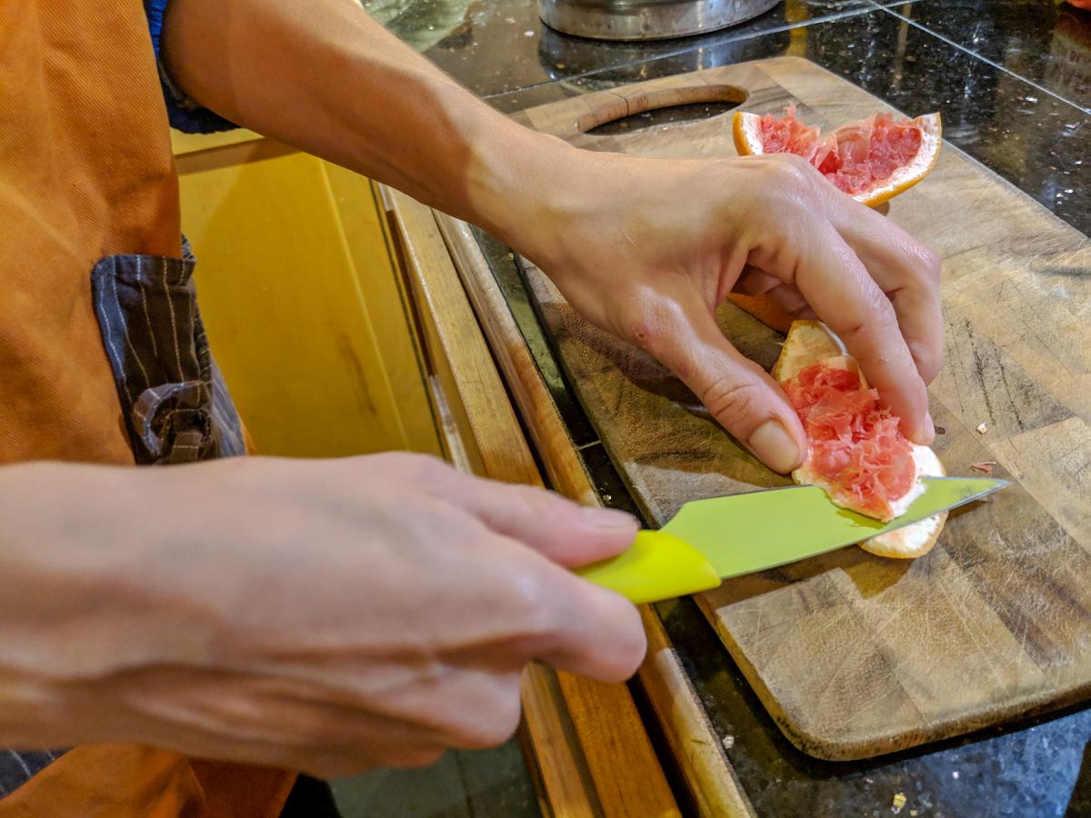 Cutting the peel from a grapefruit with a bright yellow knife. 
