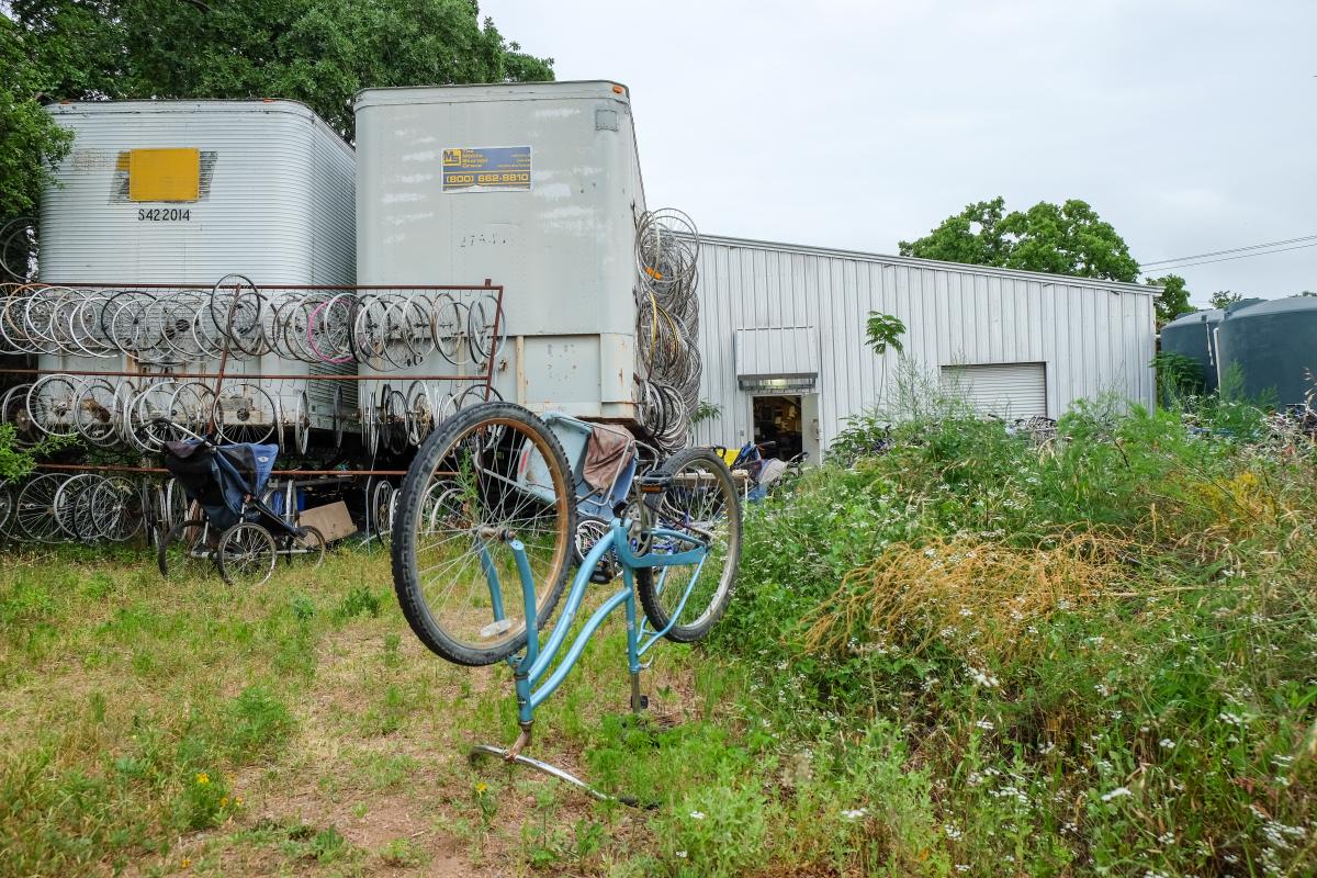 Three sheds with bicycles and wheels in front of it. In the foreground, a bicycle stands upside down.