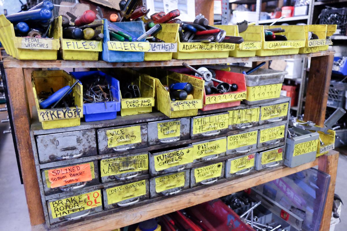 Bicycle parts in bins with yellow labels.