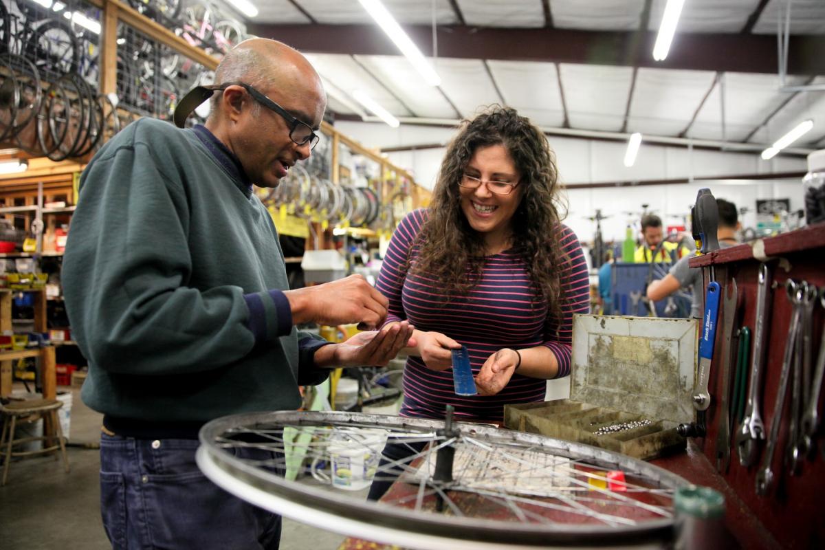 Person showing another person how to fix a bicycle wheel in a bicycle shop.